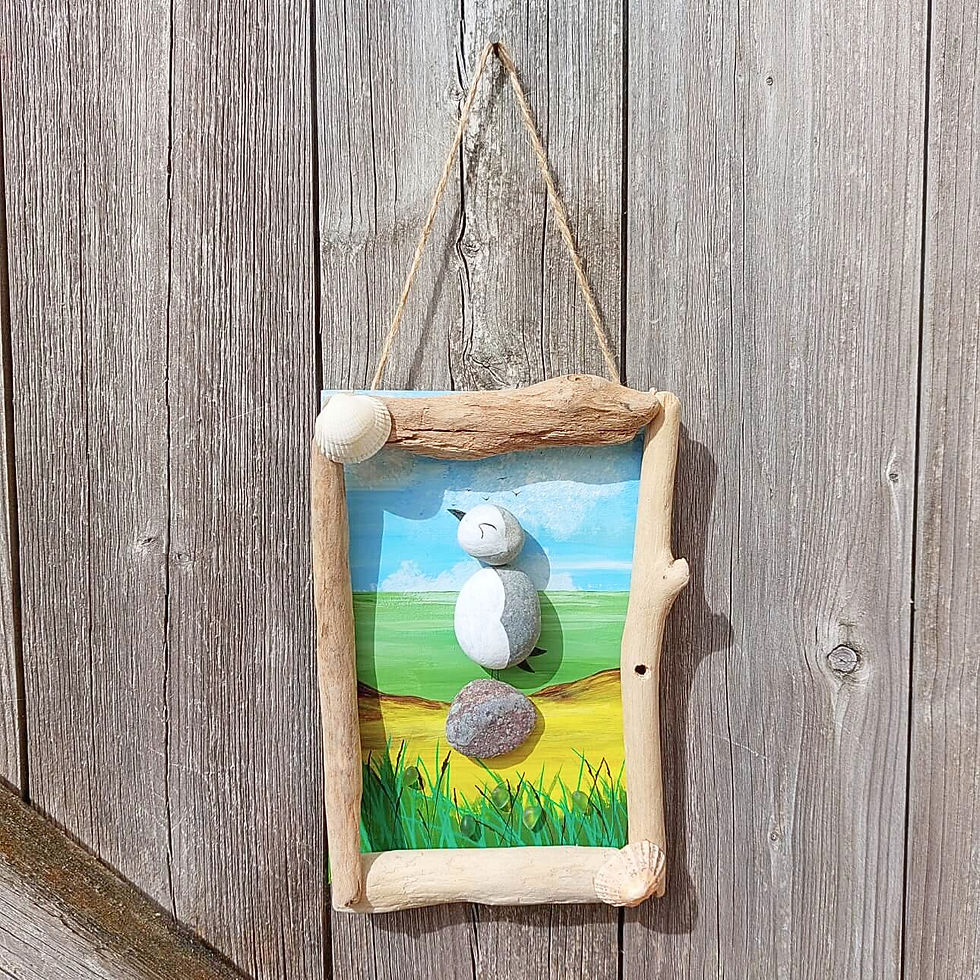 Handmade puffin hanging decoration with painted pebbles, driftwood, sea glass & shells, set against a colourful coastal scene