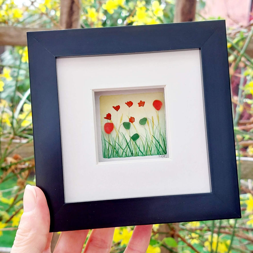Thumbnail: A black framed picture of a watercolour poppy meadow which has been embellished with red sea glass flowers.