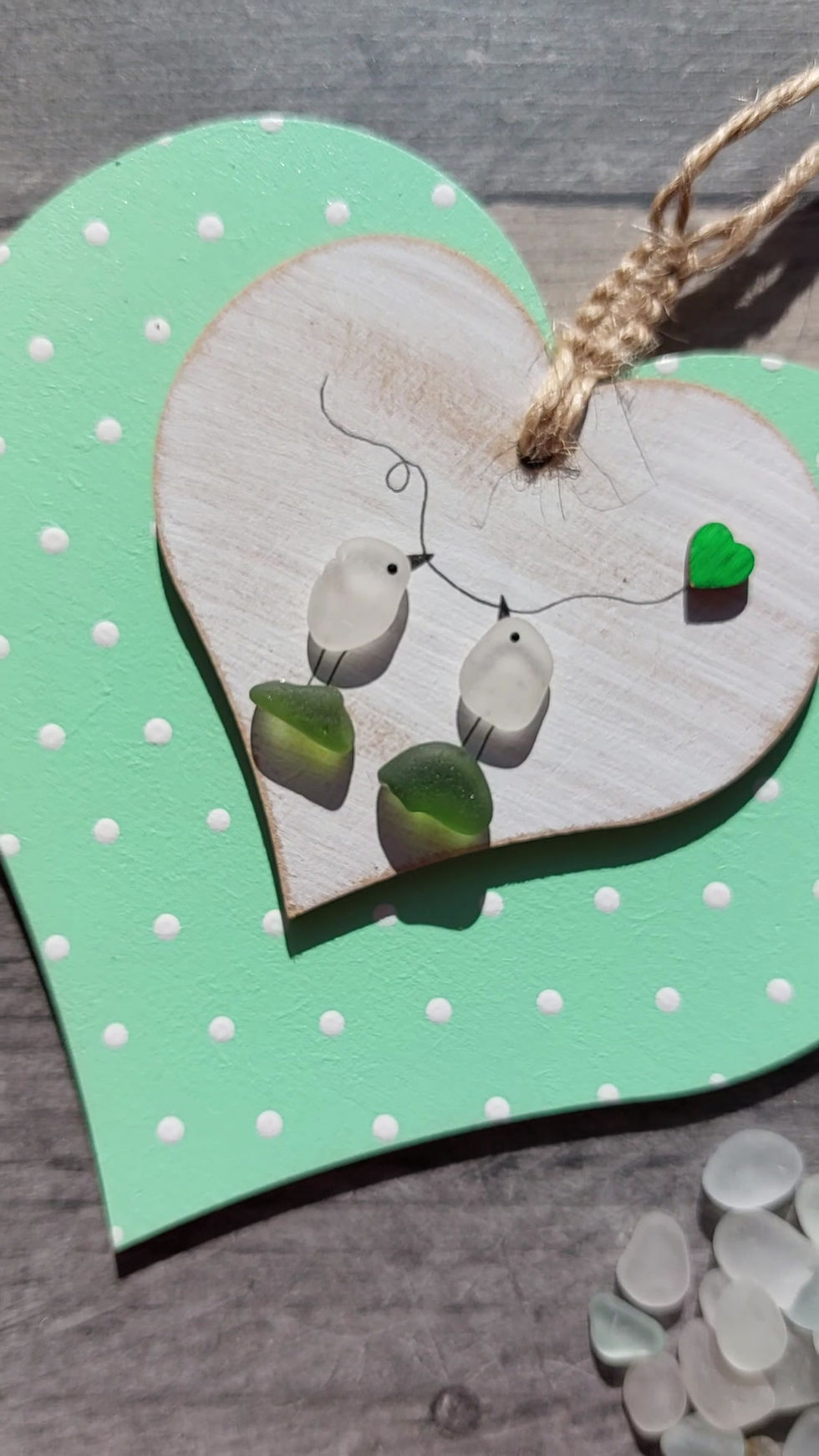 Thumbnail: A pastel green heart hanging decoration decorated with sea glass lovebirds holding a heart balloon