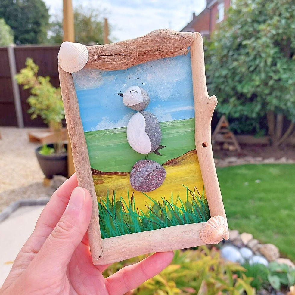 Handmade puffin hanging decoration with painted pebbles, driftwood, sea glass & shells, set against a colourful coastal scene