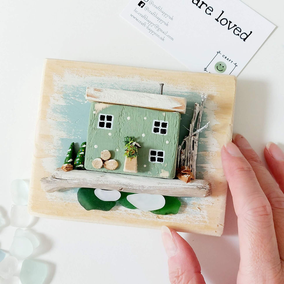Rustic wooden wall art, showing a wooden backboard, decorated with a green Christmassy cottage, with driftwood and sea glass