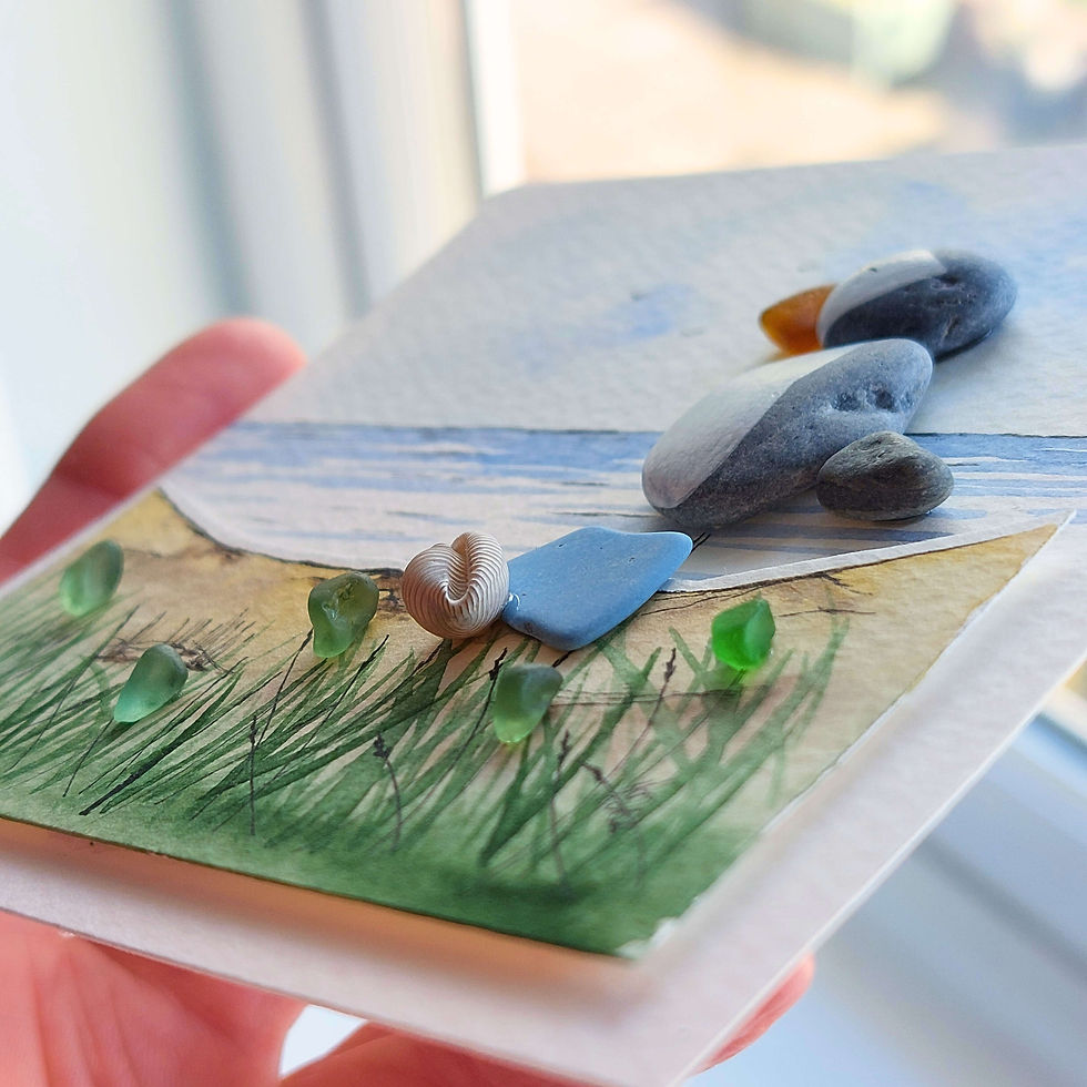 Thumbnail: A white framed hand made 3D picture of a puffin made from pebbles with sea glass below on a watercolour background.