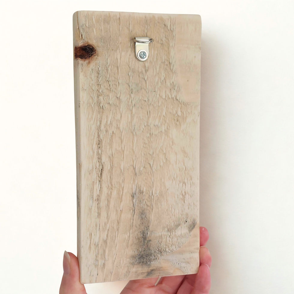 Thumbnail: A hand holding the reverse side of the piece of art against a white background. There is a hook on the reverse for hanging.