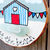 Thumbnail: A hand holding a painted wooden beach hut decoration, embellished with sea glass. The words - At the Beach - have been added