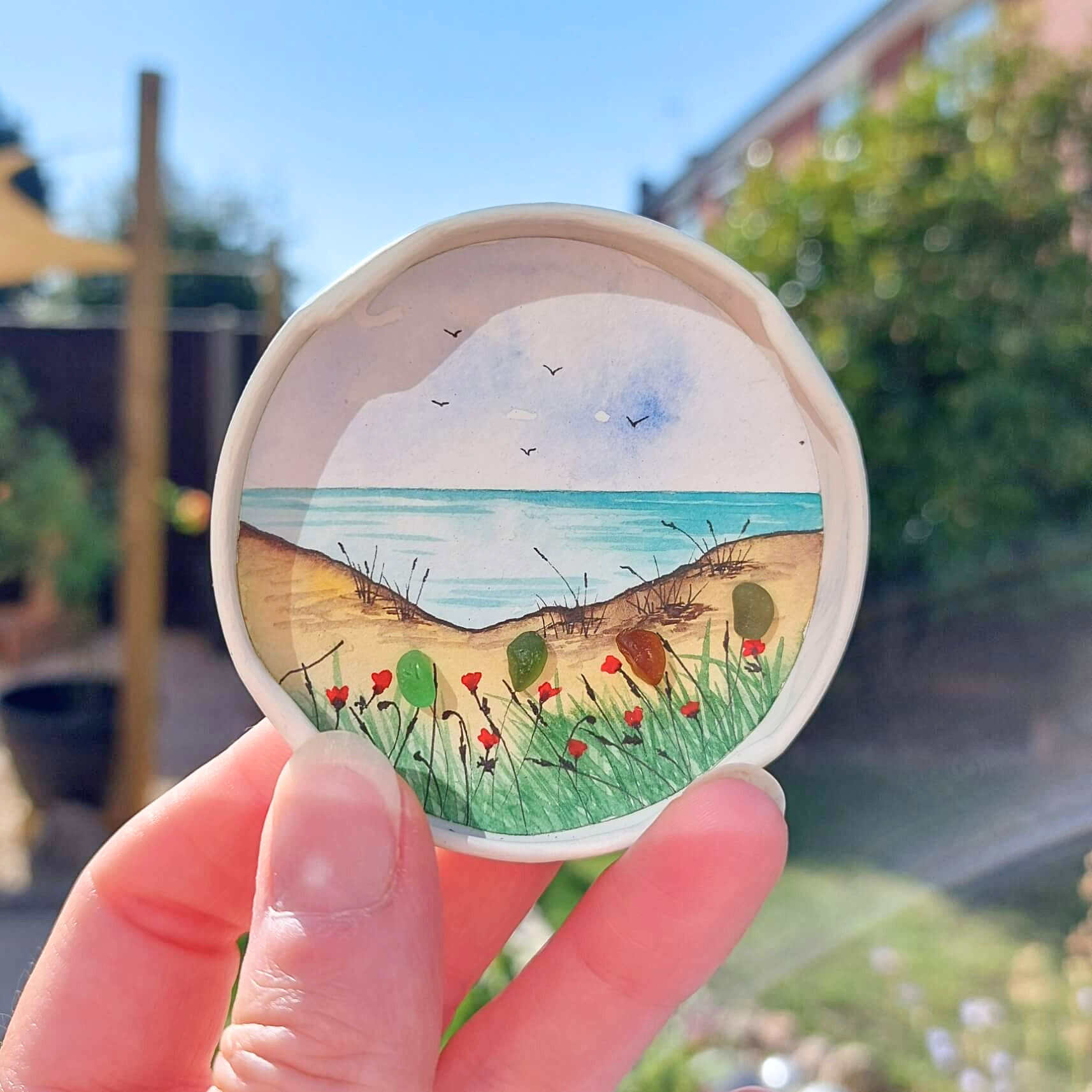 Handmade coastal fridge magnet with hand-painted beach scene, sea glass flowers and recycled red jar lid.
