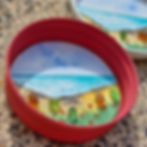 Handmade coastal fridge magnet with hand-painted beach scene, sea glass flowers and recycled red jar lid.