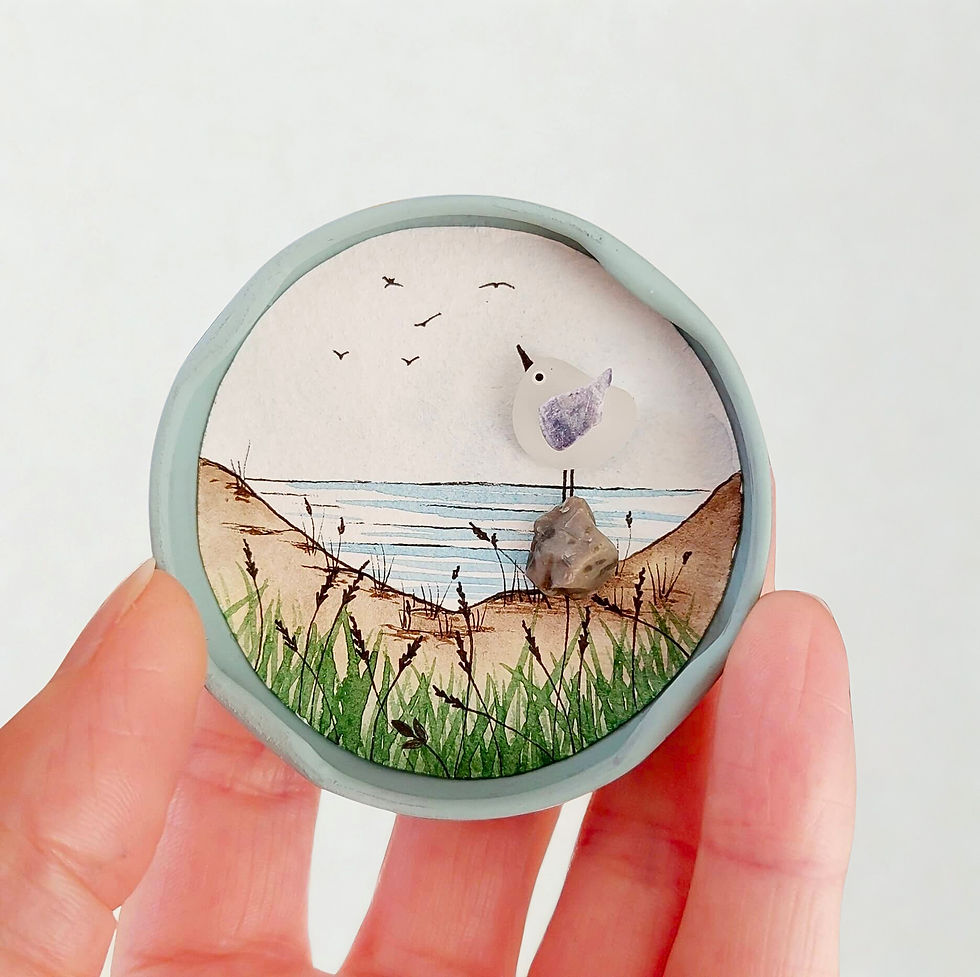 Thumbnail: A round magnet made from a recycled jar lid on a white background. Decorated with a painted coastal scene and held in a hand.