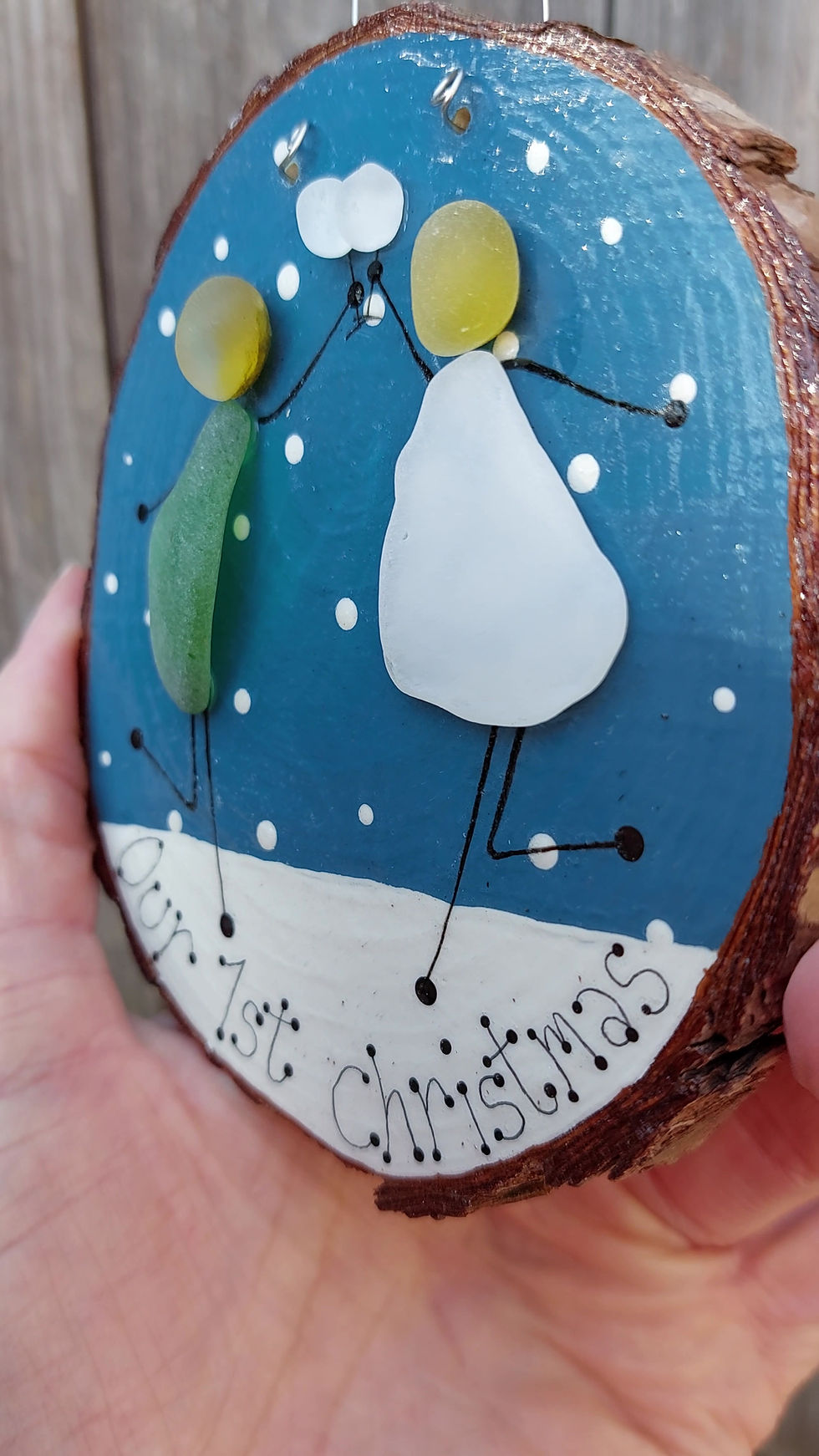 Thumbnail: A wooden decoration painted in blue and white and depicting two figures toasting with wine glasses with 'our first Christmas'