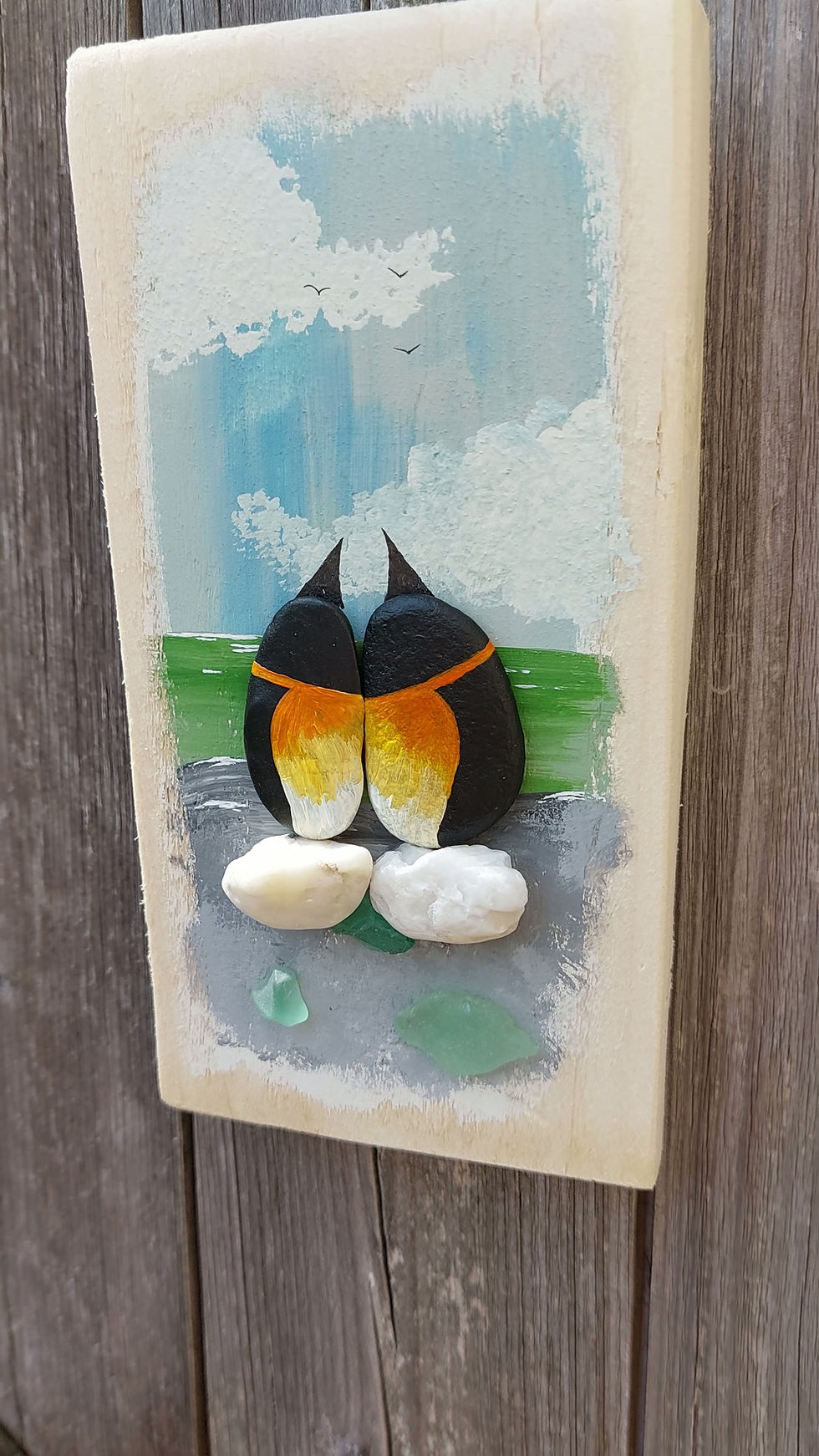 Handmade pebble penguin wall art on reclaimed wood with sea glass, shells and a hand-painted coastal scene, celebrating love.