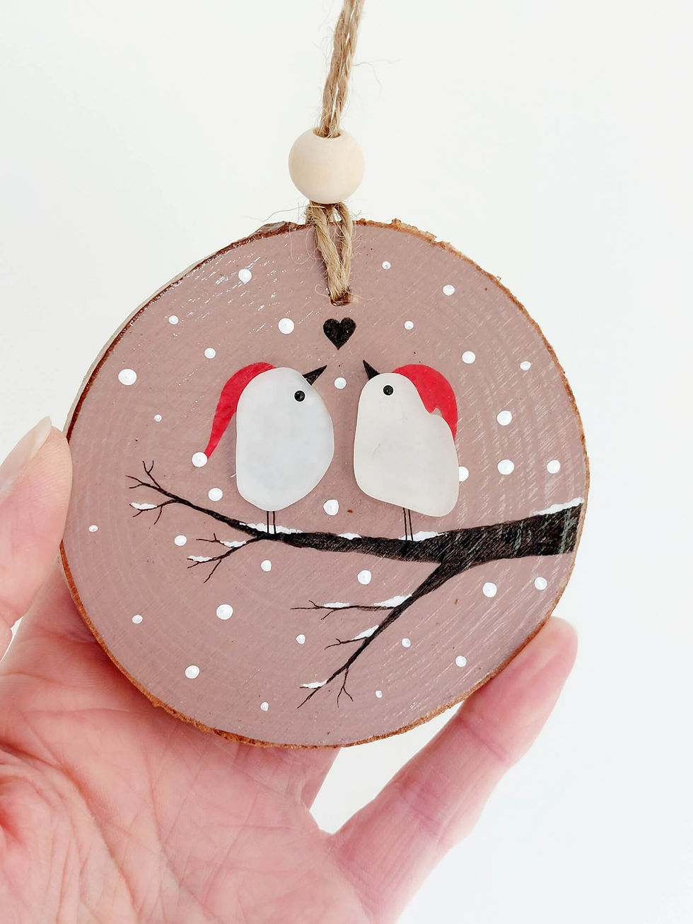 Thumbnail: A hand holding a wooden log slice, painted pink and decorated with a snowy branch on which is perched 2 birds in santa hats