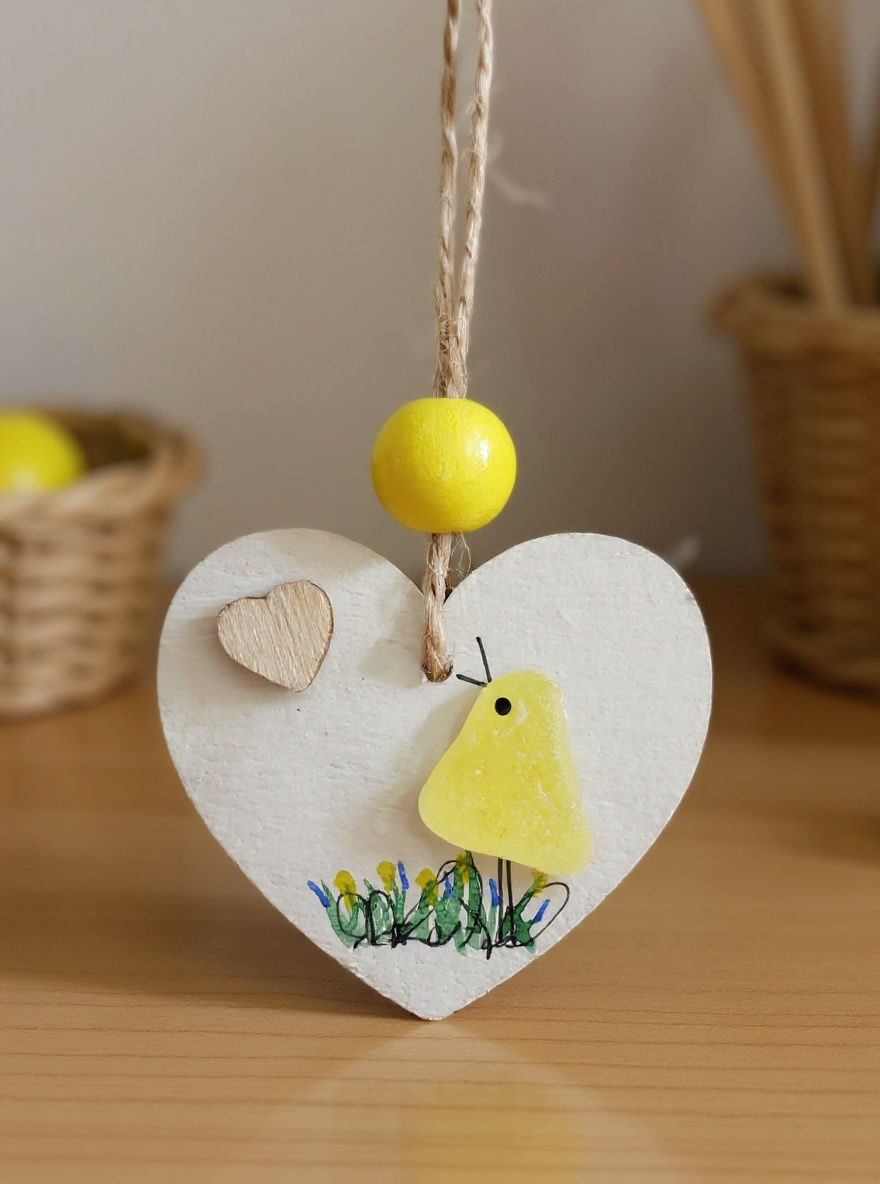 A white hand painted heart decorated with a yellow sea glass bird, watercolour details and a tiny wooden heart.