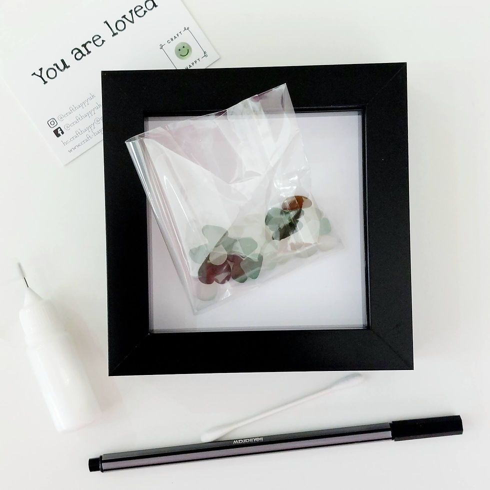 Thumbnail: The contents of a sea glass craft kit - black frame, piece of card, glue bottle, pen, bag of sea glass & instructions.