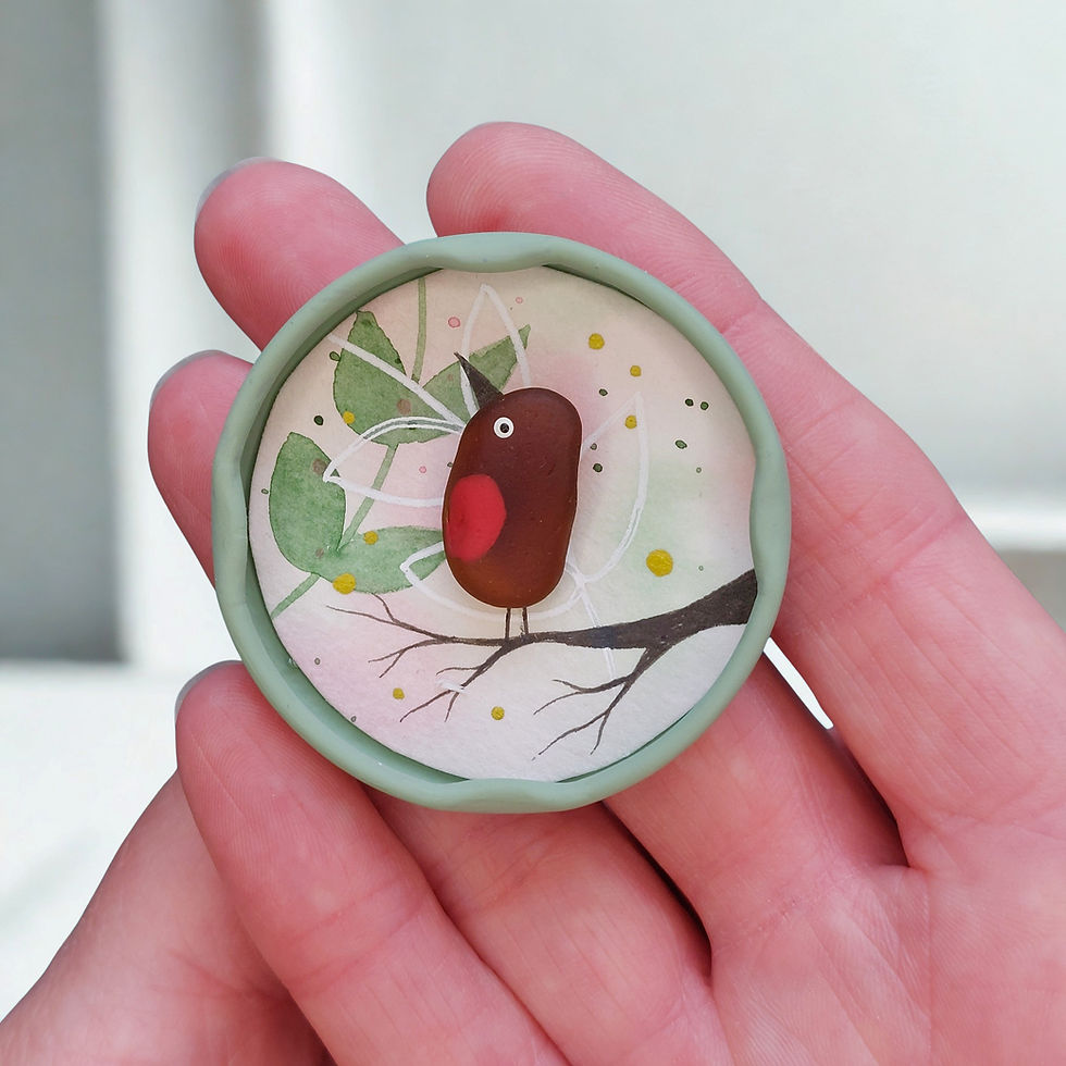 Thumbnail: A hand holding a fridge magnet made from a recycled jar lid. Decorated with a piece of brown sea glass, made into a robin.