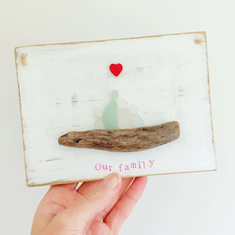 A rustic wooden picture hanging decoration showing family of 4, made from sea glass pieces, perched on a piece of driftwood.