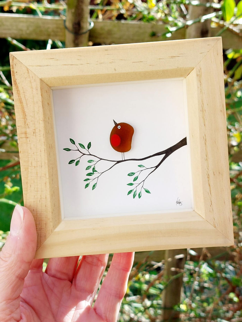 Thumbnail: A hand holding a natural pine framed picture of a sea glass robin on a hand painted branch with a twig in its beak.