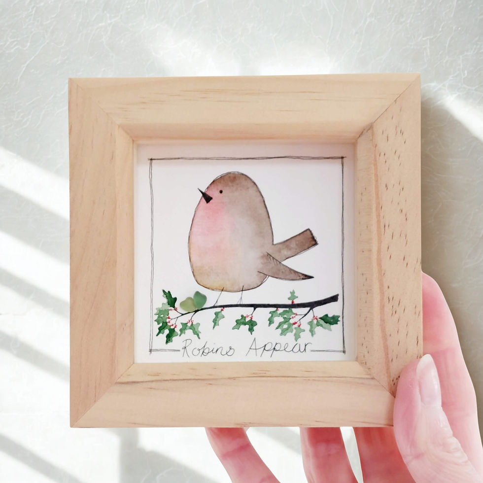 A hand holding a picture of a robin, painted in watercolours and framed in a natural pine frame.