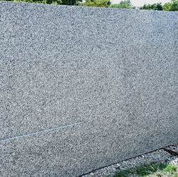 Slab of New Caledonia granite with a fine-grained mix of gray and white tones, accented by dark speckling.