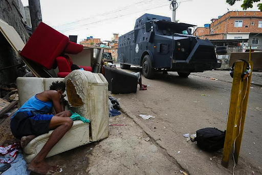 Morador dorme em sofá destruído enquanto caveirão da Polícia Civil circula pelas ruas do Jacarezinho. A operação que deixou 28 mortos em 2021 segue sem respostas efetivas do Estado. Foto: Reprodução: Fabiano Rocha/Agência O Globo.