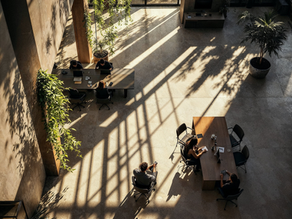 Modernes, lichtdurchflutetes Büro mit mehreren Arbeitstischen, an denen kleine Teams in entspannter Atmosphäre arbeiten – Symbol für resiliente Unternehmenskultur.