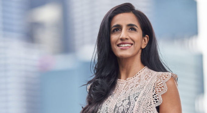 Ayesha Khanna smiles confidently against a blurred cityscape background, conveying a sense of optimism.