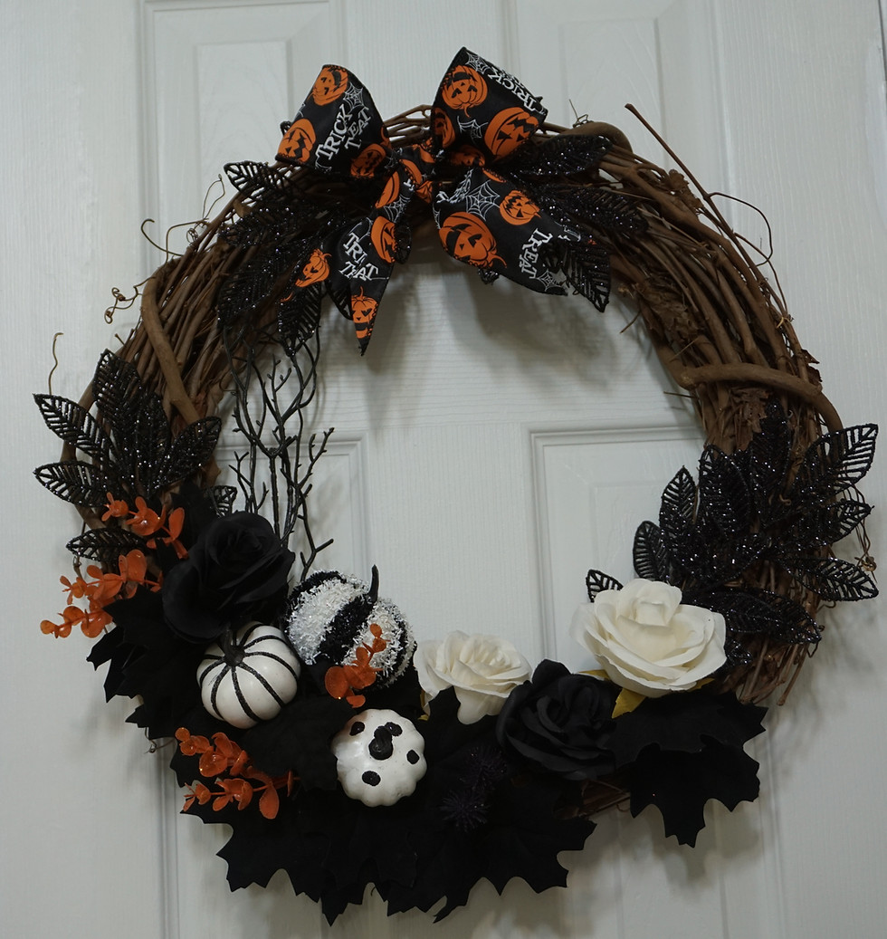 24" grapevine wreath decorated in black and orange florals. There are white and black pumpkins and black roses at the bottom.