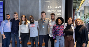 estudantes, voluntários, equipe iGUETTO e equipe Microsoft sorrindo diante do painel Microsoft Innovation Hub, em corredor moderno de escritório.