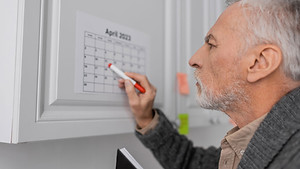 Uomo anziano che consulta un calendario segnando le date, raffigurazione visiva dei sintomi cognitivi dell'Alzheimer.