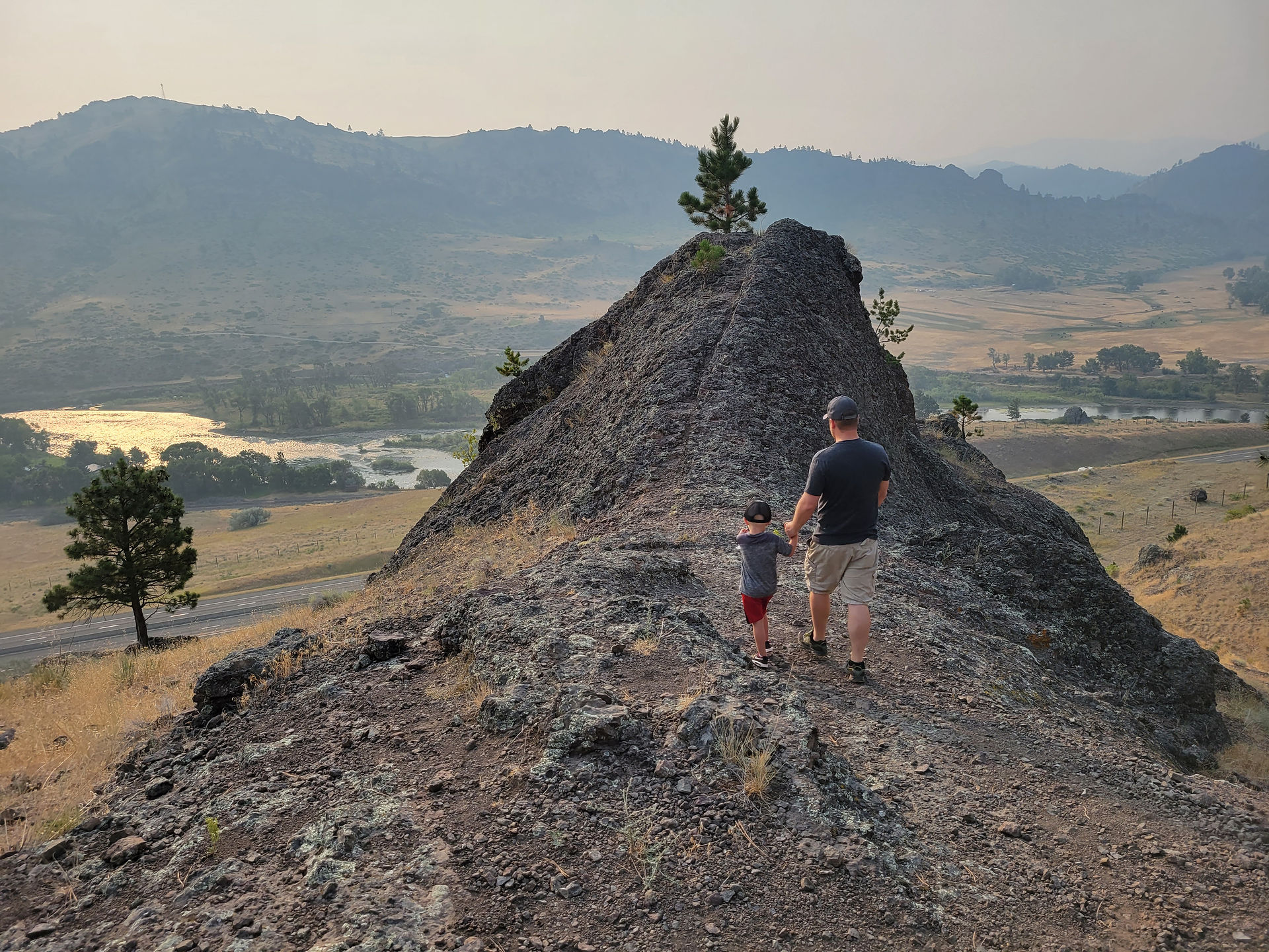 Little boy and father stand at the edge of a rock overhang looking out over the river at Tower Rock State Park, Montana.