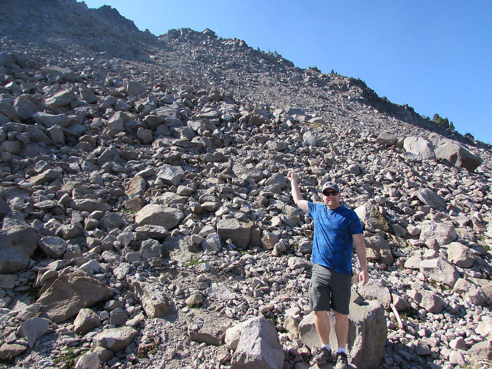 Man pointing up the rocky hillside towards the Watchman Lookout Tower in Crater Lake National Park