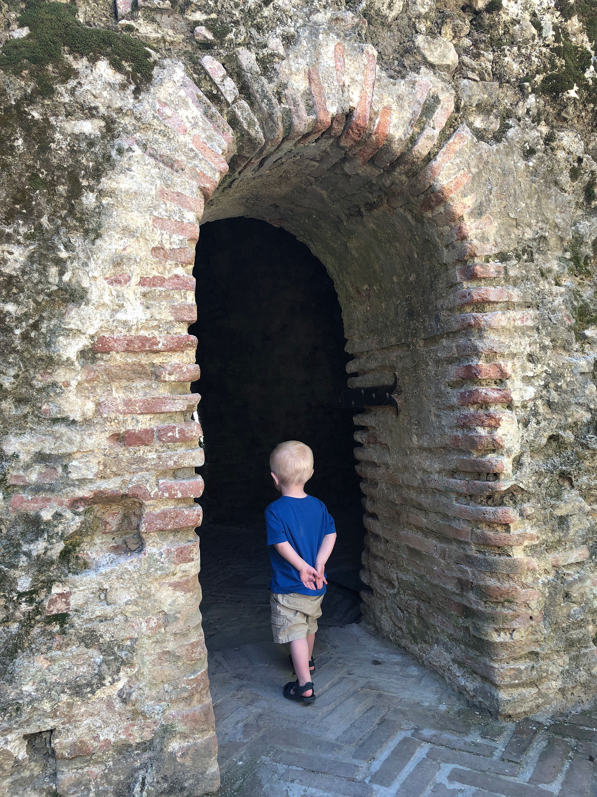 Little boy stands looking into a dark arched entryway inside the Arab Baths in Ronda, Spain.