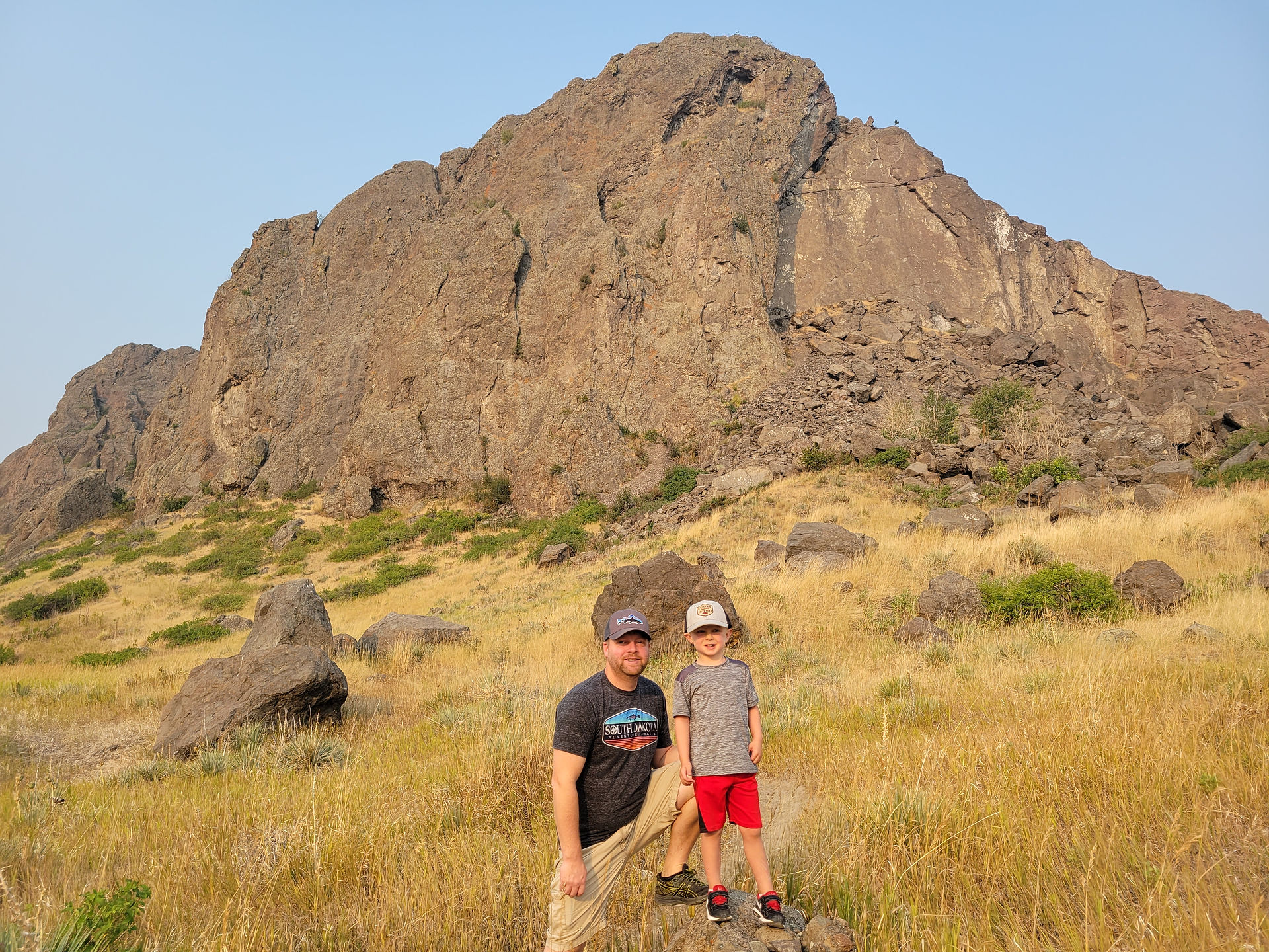 Father and son stand in front of the giant Tower Rock at Tower Rock State Park in Montana.