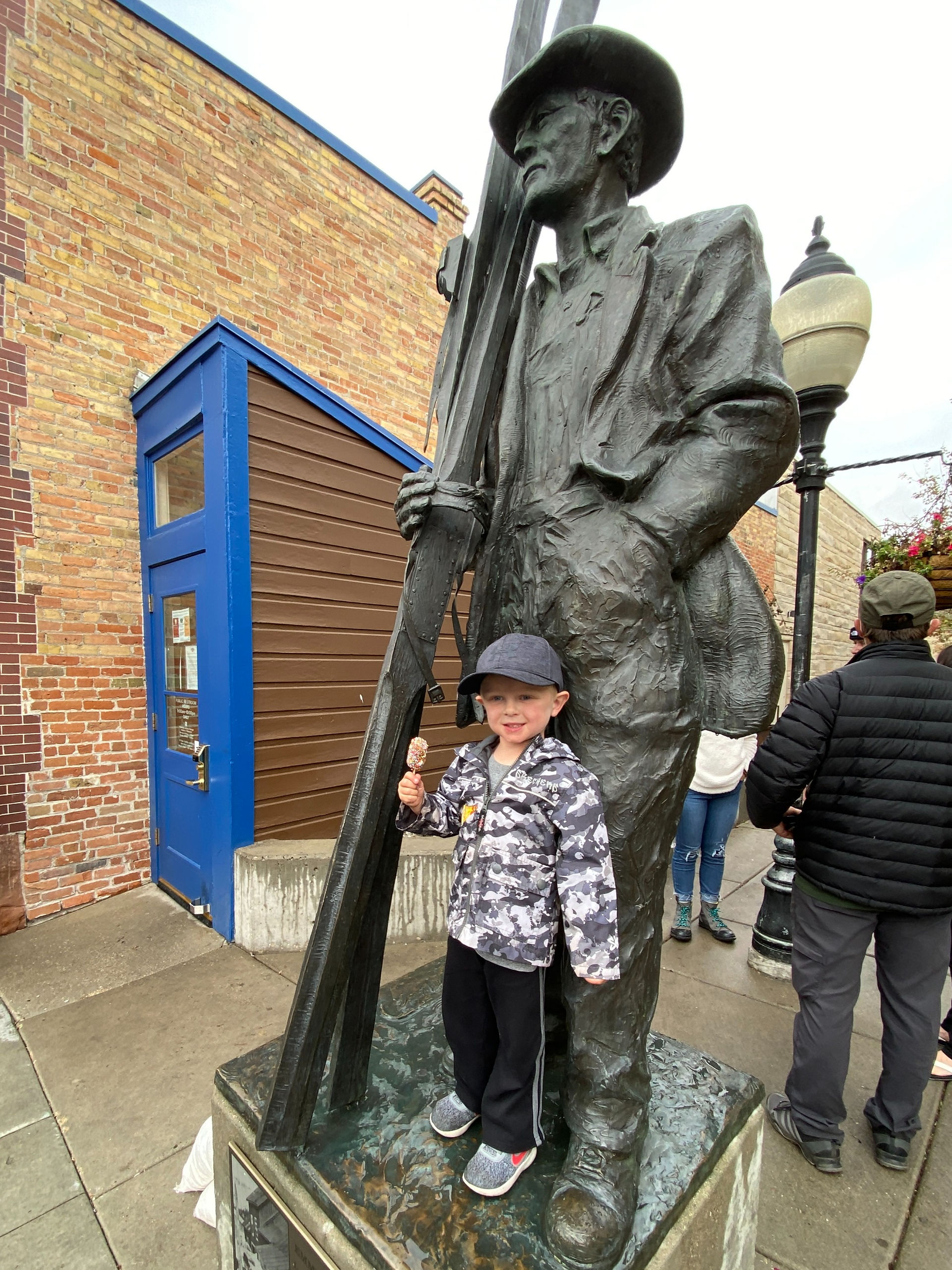 Little boy standing next to a ski statue in downtown Park City, Utah.