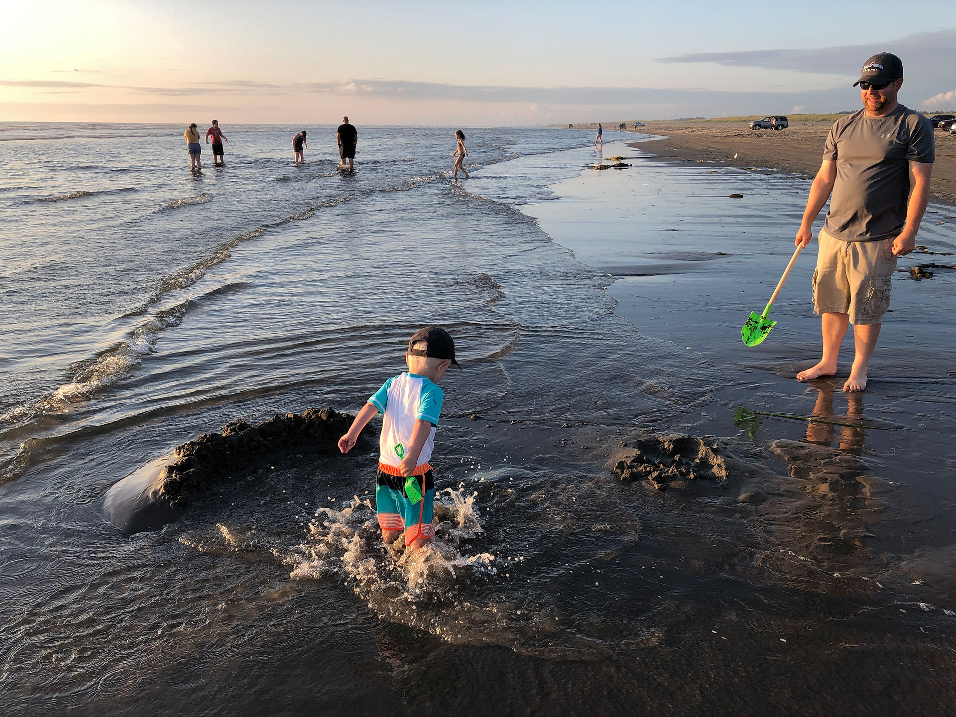 Little boy splashing in the water's edge on the sandy beach of Long Beach, Washington while dad watches.