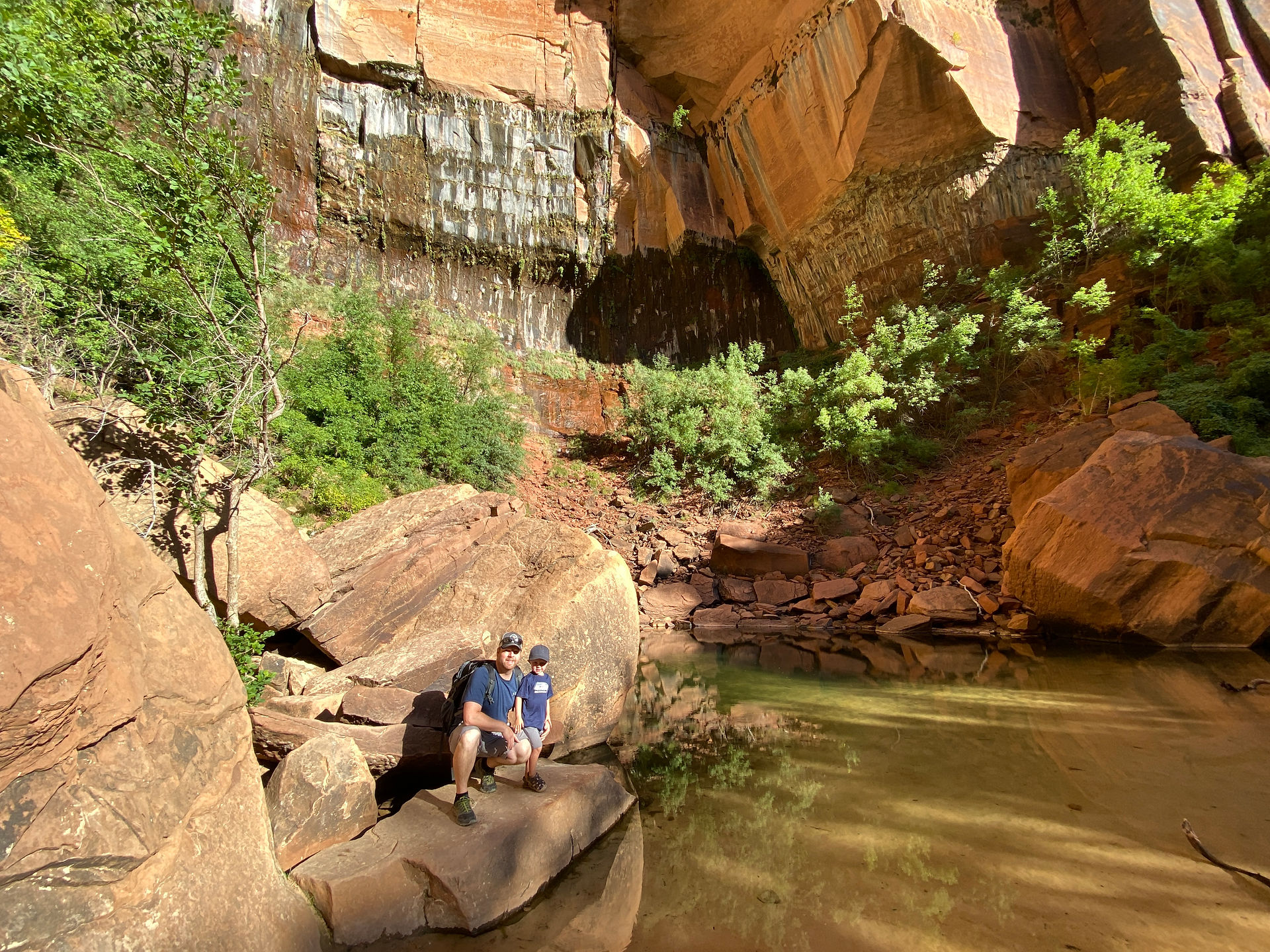Father and son stand on a large rock near Upper Emerald Pool in Zion National Park.