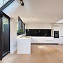 A newly renovated kitchen with white surfaces and shiny black cupboards.jpg