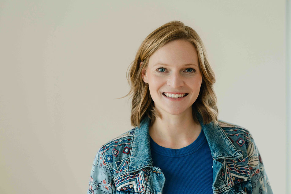 Schlafcoach und Psychologin Dr. Sarah Castiritus mit schulterlangem, hellbraunem Haar lächelt in die Kamera. Sie trägt eine gemusterte Jeansjacke über einem blauen Hemd und steht vor einem schlichten, hellen Hintergrund.