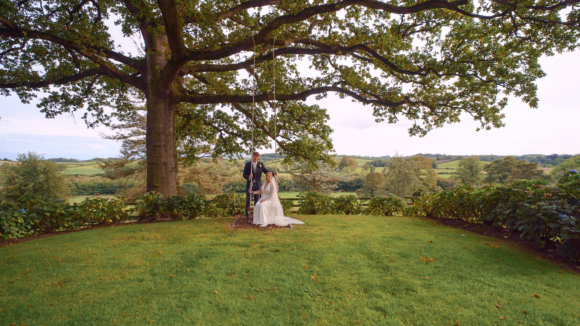 A bride and groom sharing an embrace surrounded by lush tress and greenery. A bride and groom standing in front of two wedding cars which are parked at the front of a Georgian style wedding venue. Taken at Northern Ireland wedding venue Tullyveery House by Northern Ireland Photographer and Videographer Steenson Film and Photography.