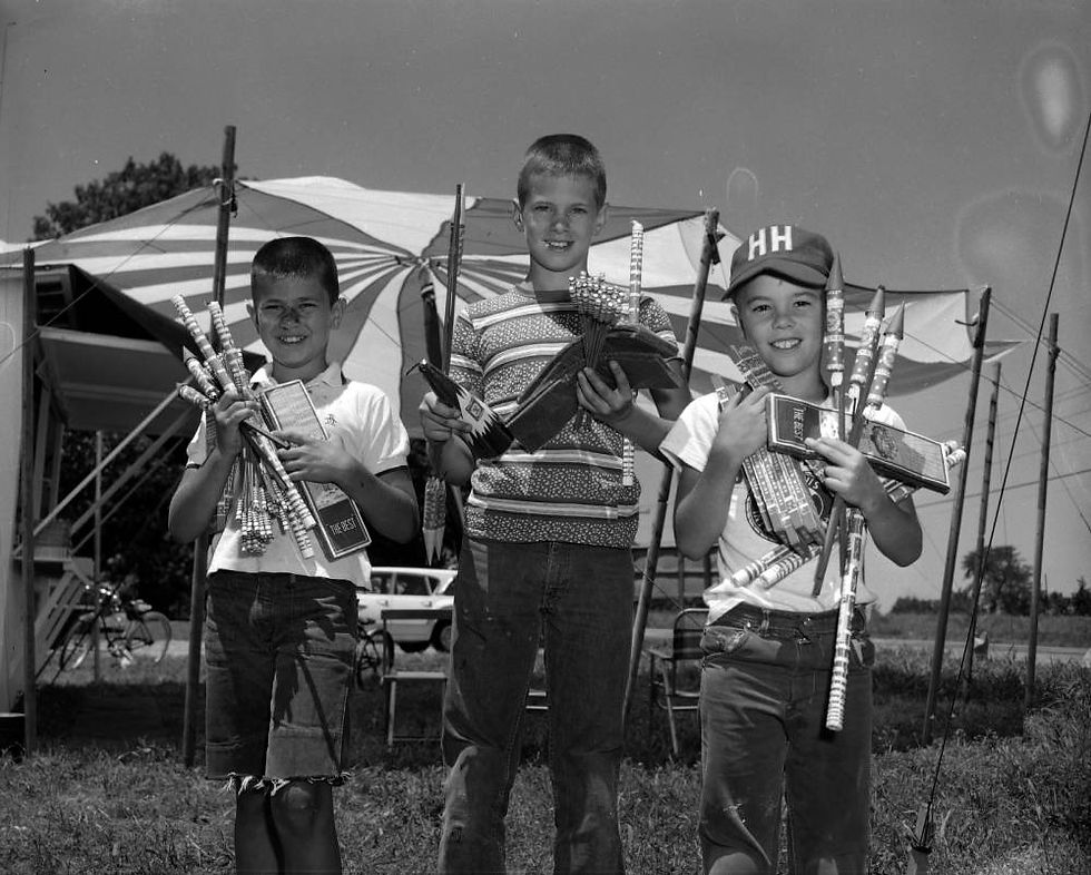 A black and white photograph of three young boys holding fireworks.