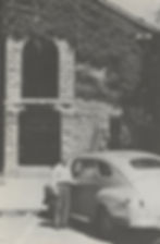 Douglas Mahnkey stands next to a car in front of the 1855 Taney County Courthouse in Old Forsyth. The front of the building is covered in ivy.