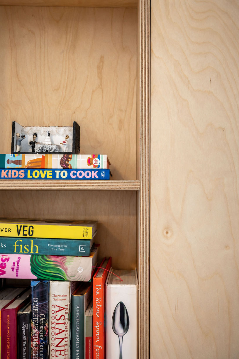 Timber joinery detail with recessed shelves holding cookbooks beside a tall cupboard door.