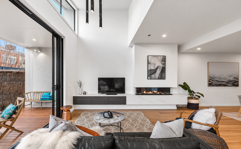 Double-height living room with clerestory glazing, integrated fireplace and direct connection to the outdoor deck.