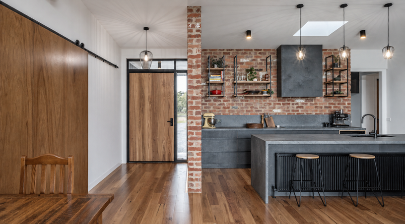 Open-plan kitchen and entry with recycled brick walls, timber flooring and dark grey island joinery.