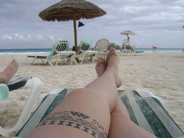 Woman displaying a Hawaiian leg and thigh tattoo with Polynesian kakau motifs, designed by King ‘Afa in 2009. hawaii tattoo leg band thigh high hawaii beach