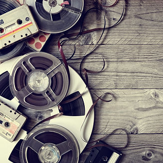Reel-to-reel tapes and cassettes on wood table, loose tape exposed – vintage audio conversion media