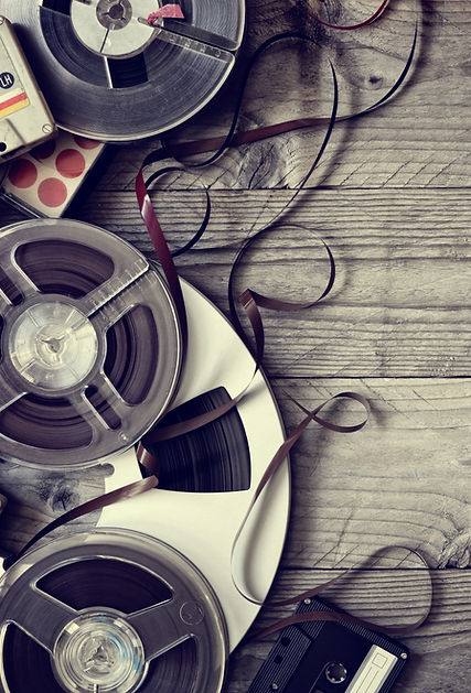 Reel-to-reel tapes and cassettes on wood table, loose tape exposed – vintage audio conversion media