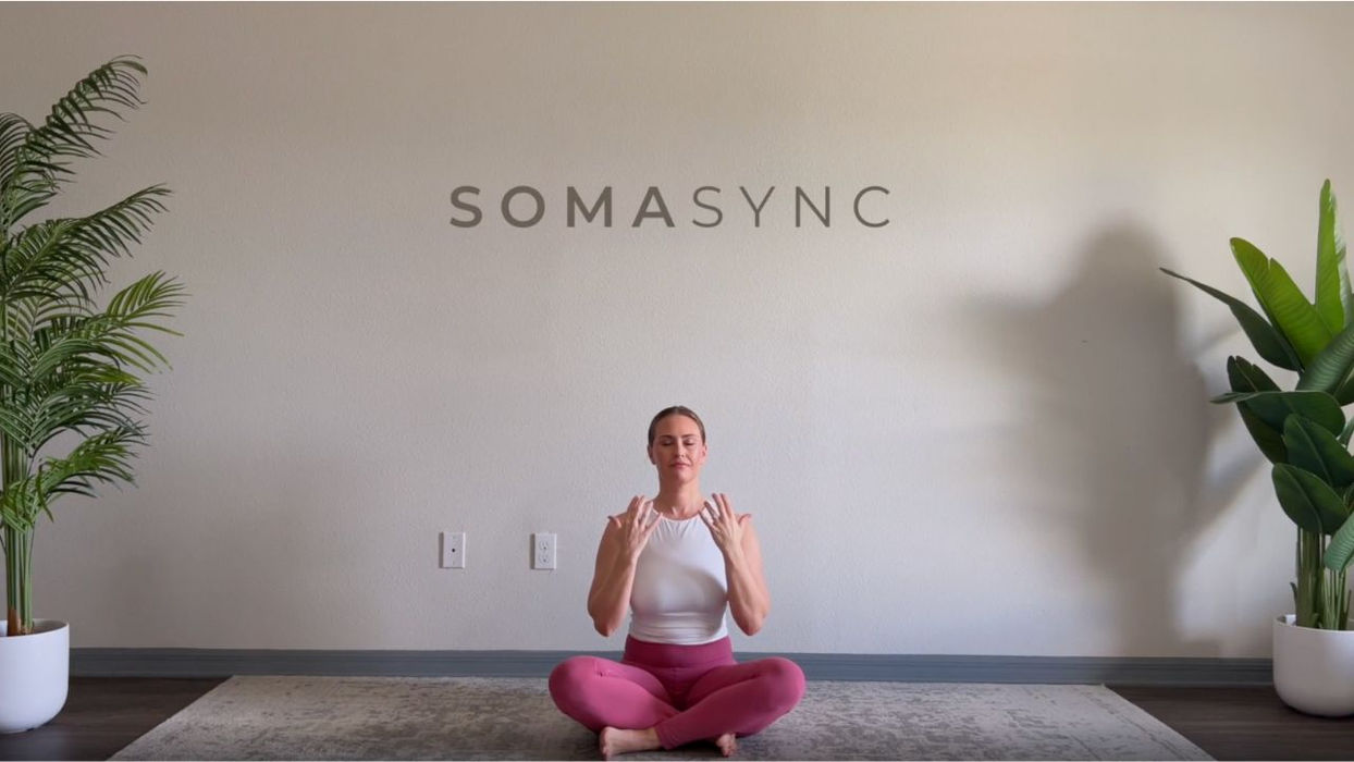 Woman sitting cross-legged, hands near shoulders, SOMASYNC text above.