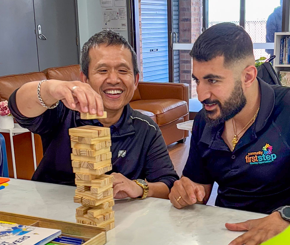 Two men play Jenga at a table, smiling and focused. One is reaching for a block.