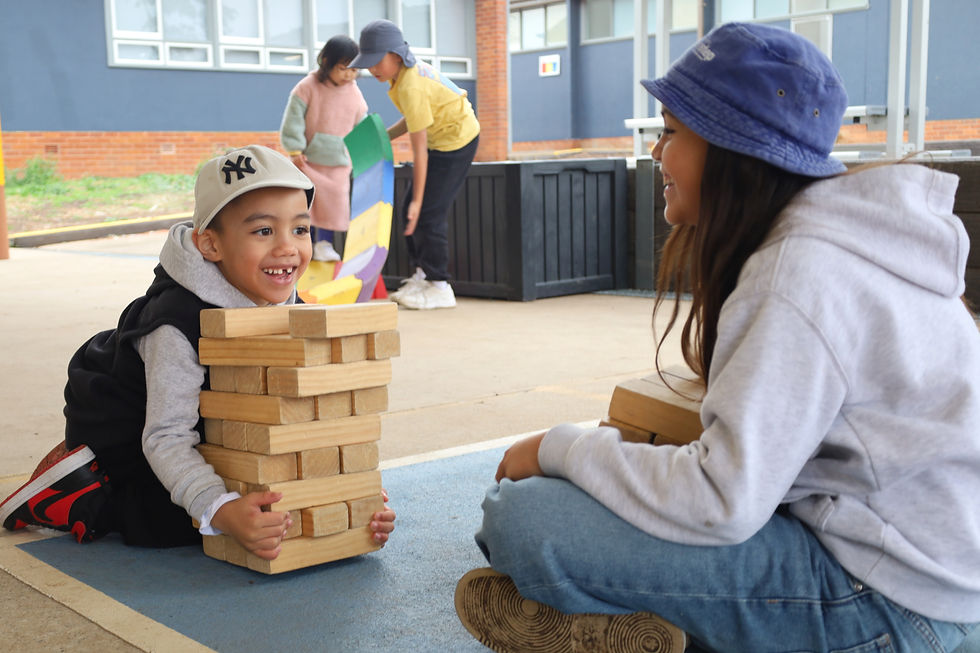 Child and educator playing with wooden blocks outdoors, smiling.