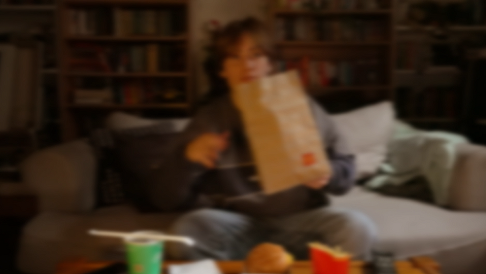 Person opening fast food bag while sitting on a couch at home.