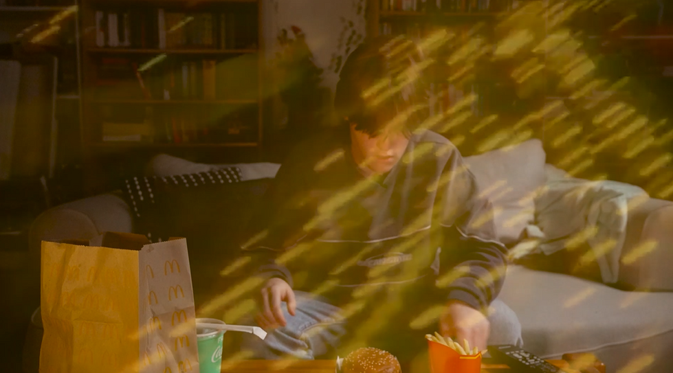 Young person enjoying McDonald's meal on a couch, surrounded by lights.